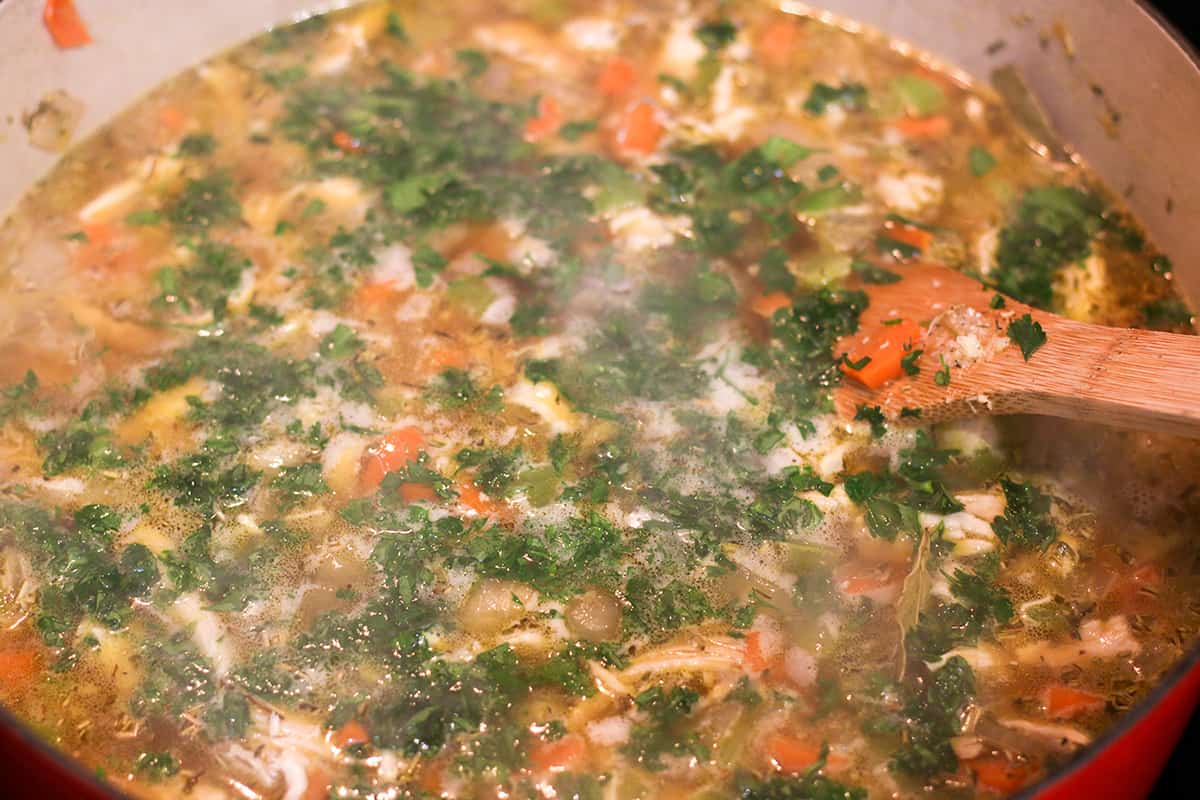 Dutch oven cast iron pot with chicken noodle soup and fresh parsley. 