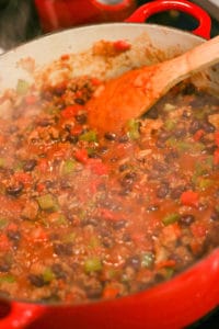 adding liquid to a homemade chili in a dutch oven