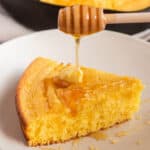 A plate with a wedge of cornbread with butter and honey being drizzled on.