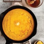 A cast iron pan with cornbread topped with butter and sides of butter and honey.