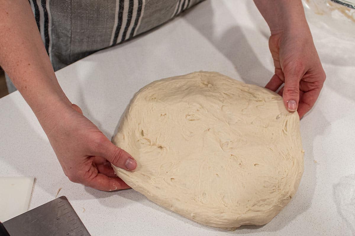 The fist step in shaping a loaf of sourdough. Two hands carefully stretching and flattening out the dough. 