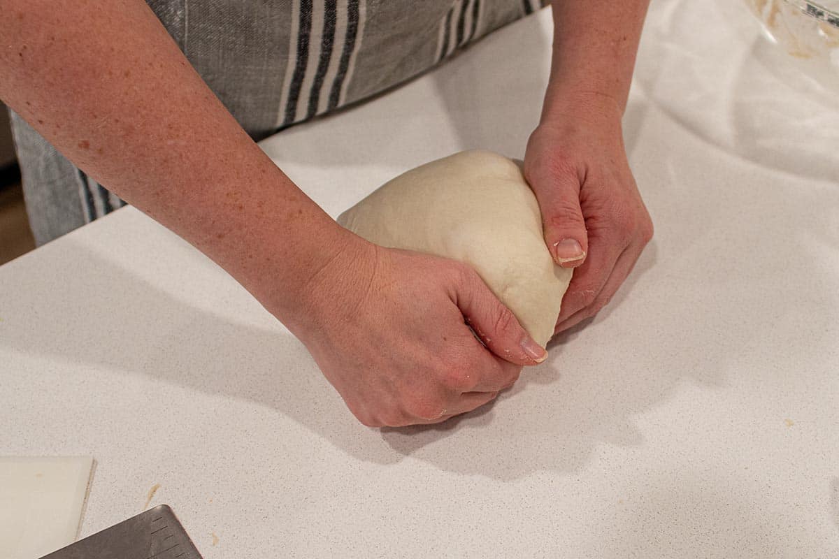 Two hands doing the final shaping of a loaf of sourdough bread.