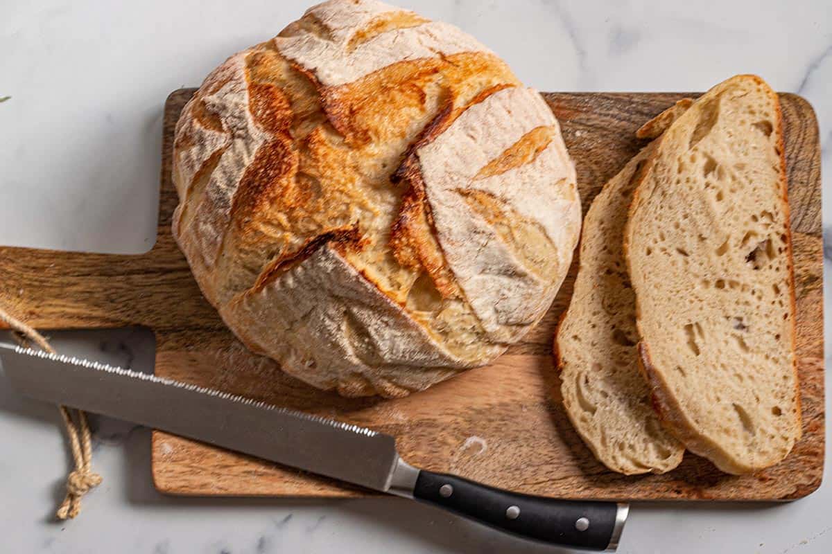 Loaf of sourdough bread on a wooden board with a serrated knife. 