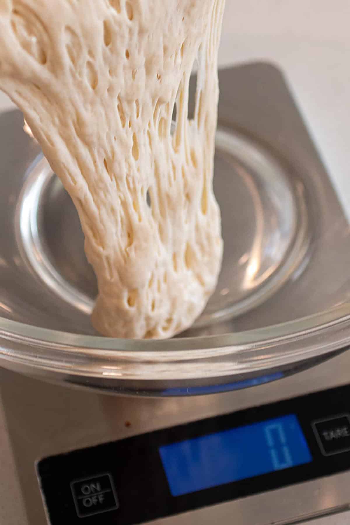 Sourdough starter being poured into an empty glass bowl on a zeroed out digital scale.