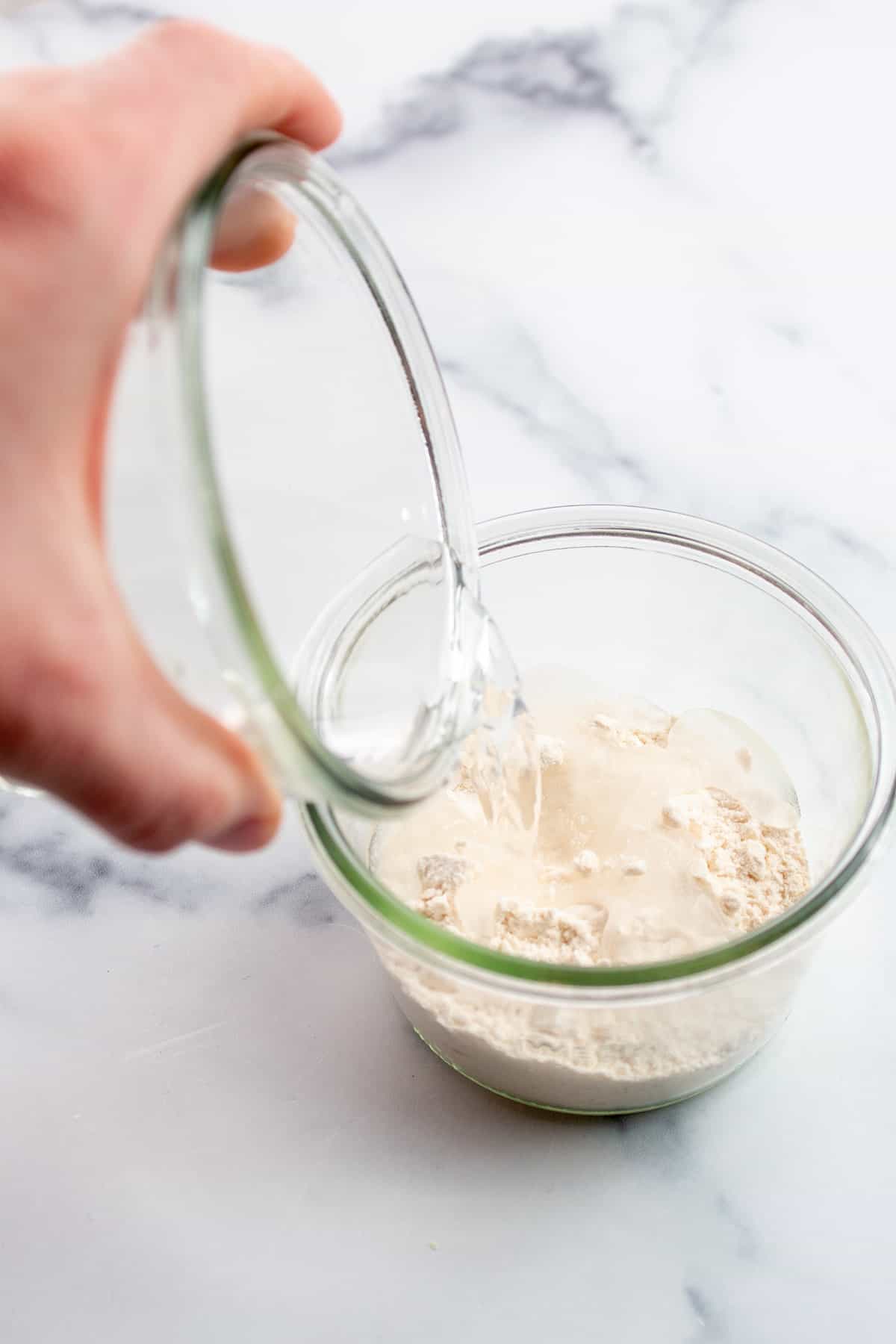 Two glass jars. one with flour and the other with water being poured into the flour.