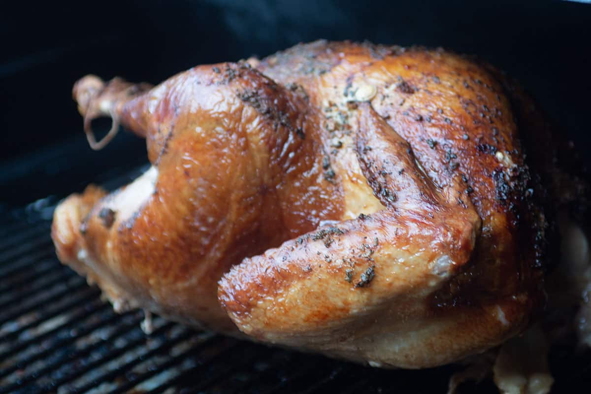 A smoked turkey with sitting on the grate of a grill.