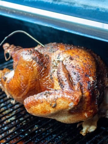 A large turkey with a temperature probe sitting on a grill grate of a smoker.