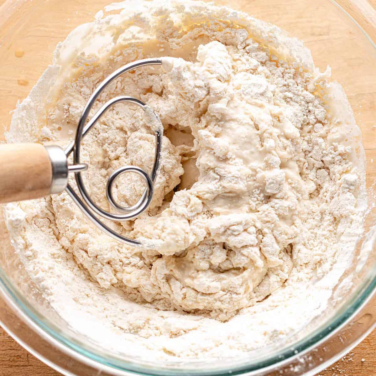 A glass bowl with a sourdough starter and danish dough whisk mixing it together.