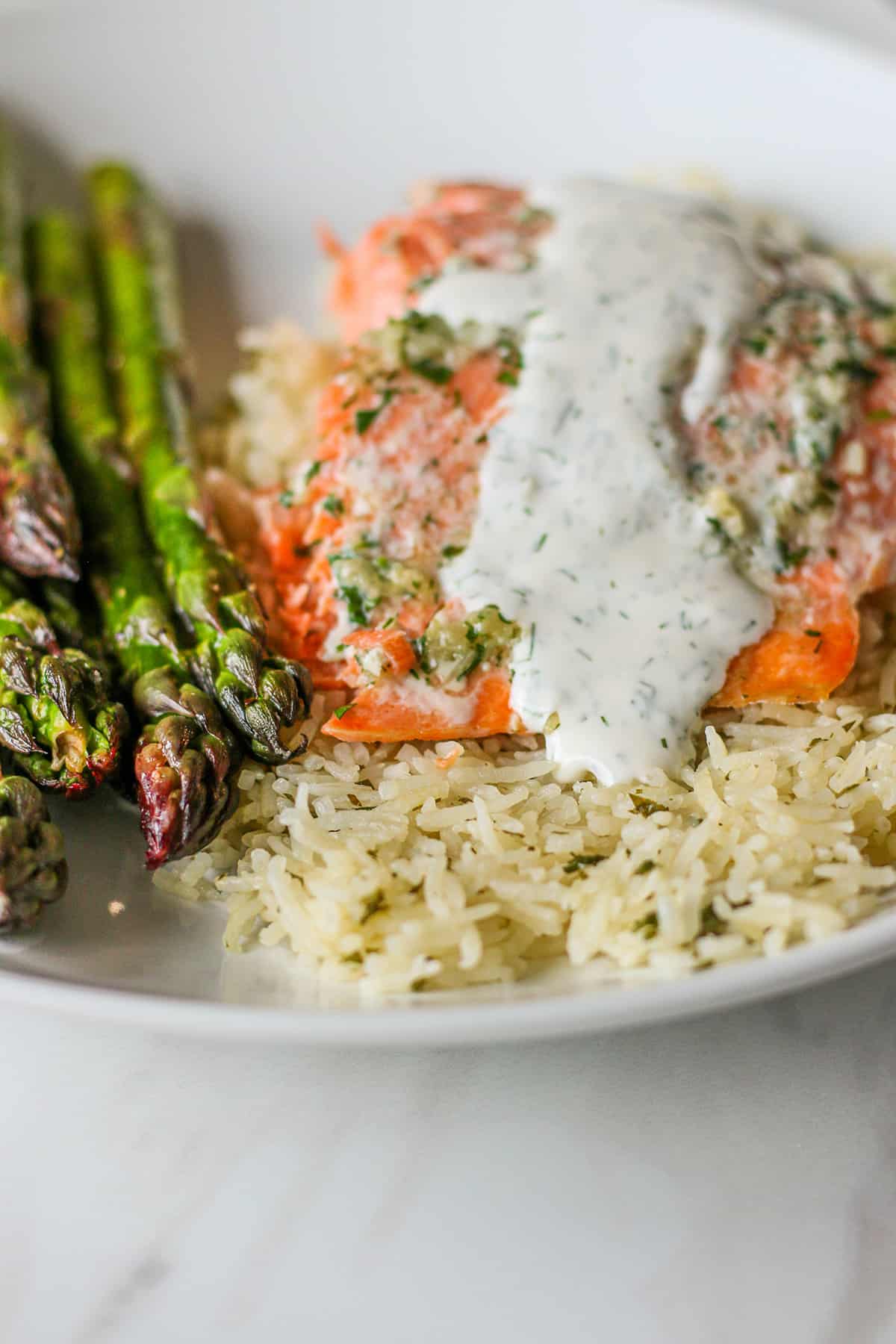 Plate with fresh salmon, asparagus, rice topped with sauce. 