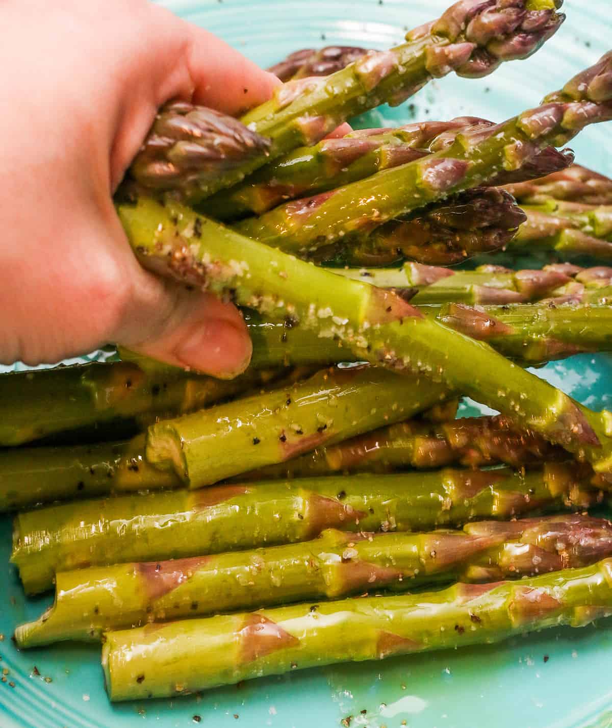 A hand tossing asparagus in oil and salt and pepper.