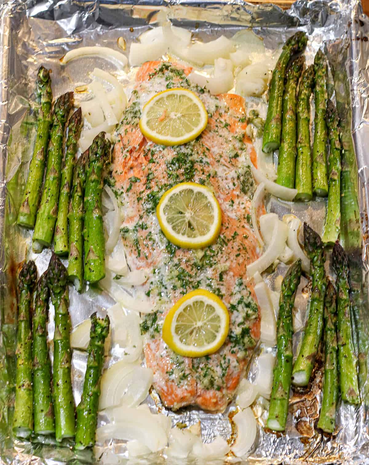 Sheet pan with salmon asparagus lemon and fresh herbs. 