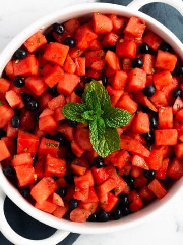 A white serving tray with cubed watermelon, blueberries and fresh mint on top.