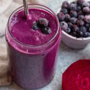 Glass cup with a purple smoothie, metal straw and frozen blueberries.