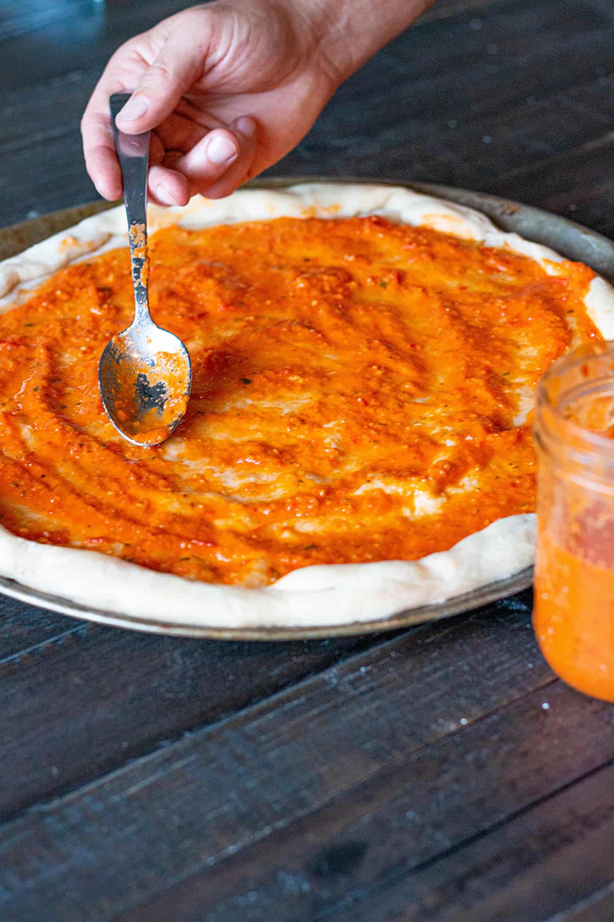 Fresh homemade pizza dough with homemade pizza sauce being spread on it. 