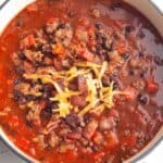 A white Dutch Oven full of a chili made with ground beef, black beans and bacon.