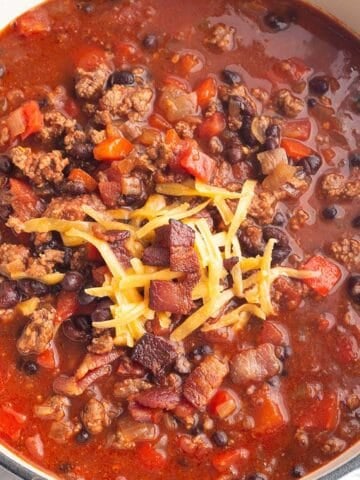 A white Dutch Oven full of a chili made with ground beef, black beans and bacon.