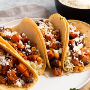 A plate with four tacos filled with rice, sweet potatoes, and black beans.