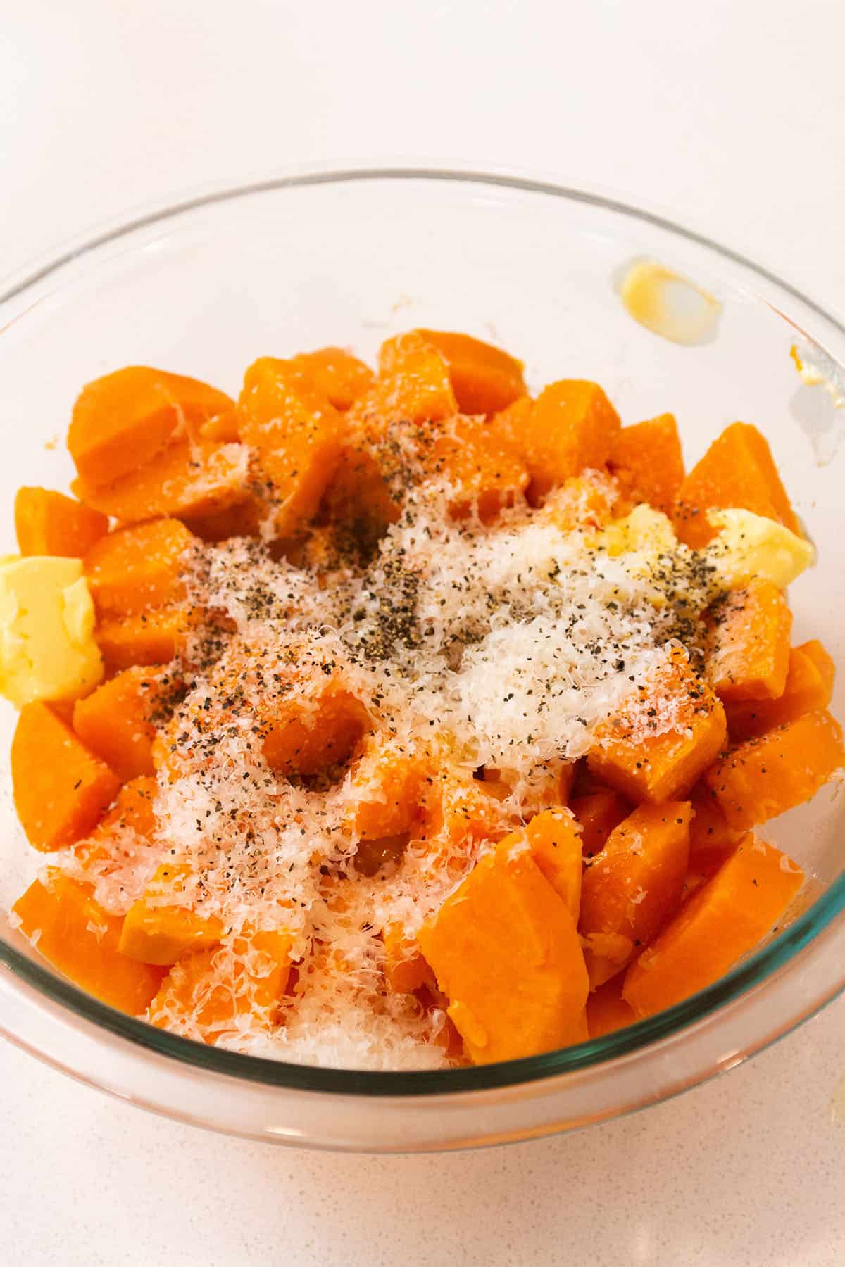 A bowl with soft sweet potatoes, butter, parmesan cheese, salt and pepper. 