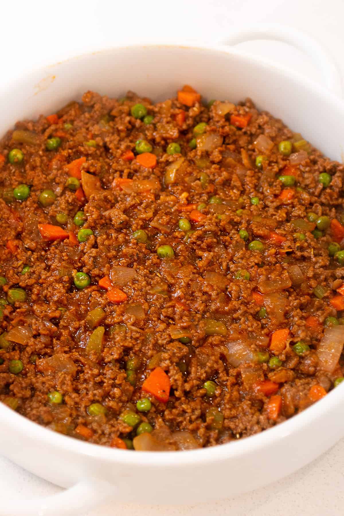 A circular white baking dish with a ground beef and veggie mix. 