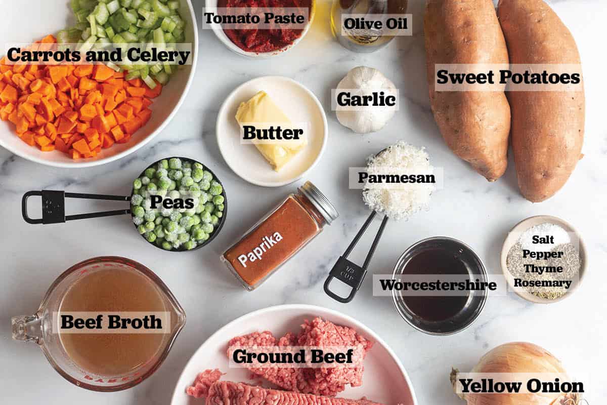 Ingredients laid out for a sweet potato Shepherds pie. Sweet potatoes, seasoning, parmesan cheese, ground beef, onion, beef broth, worcheschire, carrots, peas, celery, tomato paste and olive oil. 