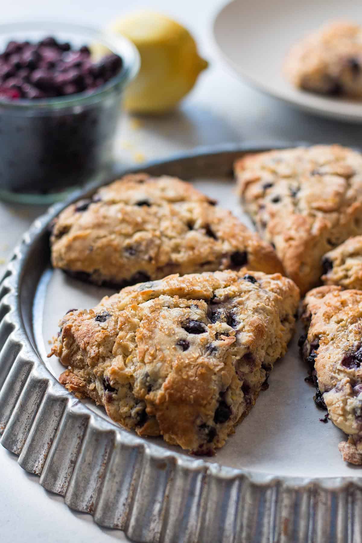A tin tray with blueberry lemon scones. Frozen blueberry and a lemon in the background.