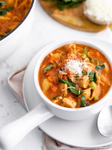 A handled soup bowl with a tomato soup with chicken, basil and parmesan.