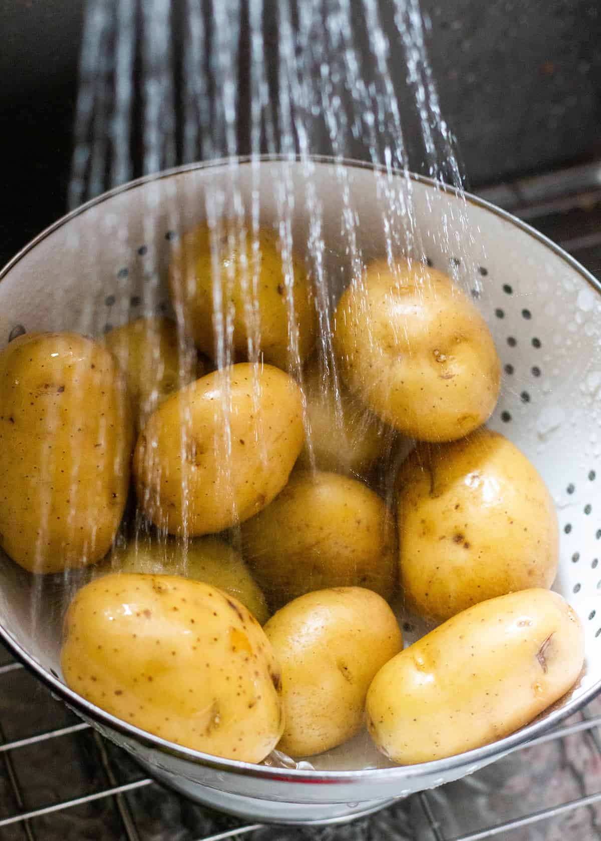 Yukon Gold Potatoes being washed in a collander under running water.