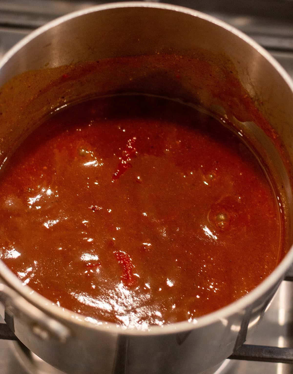 Homemade enchilada sauce simmering on a stove top.