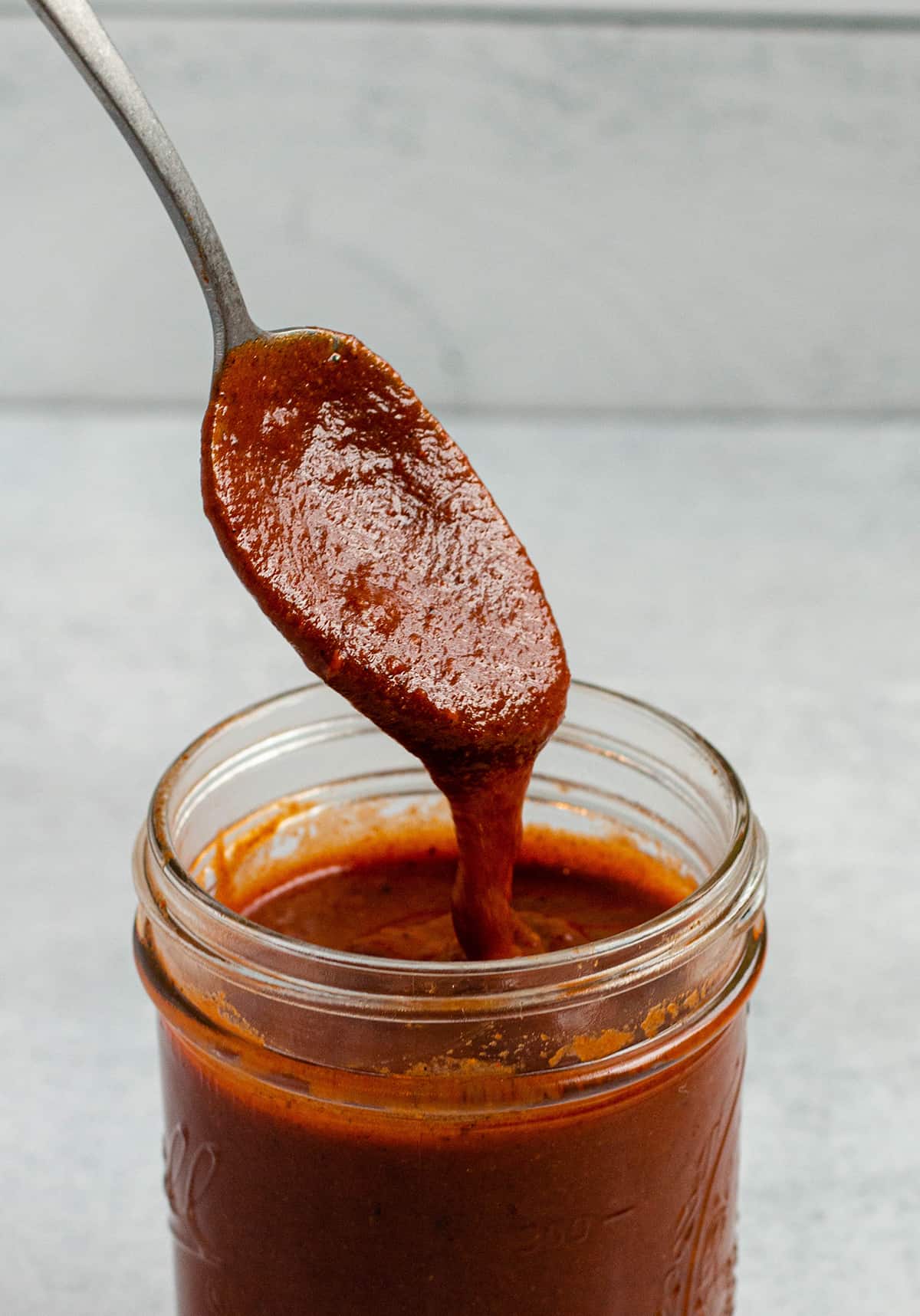 Spoon scooping out homemade enchilada sauce from a jar.