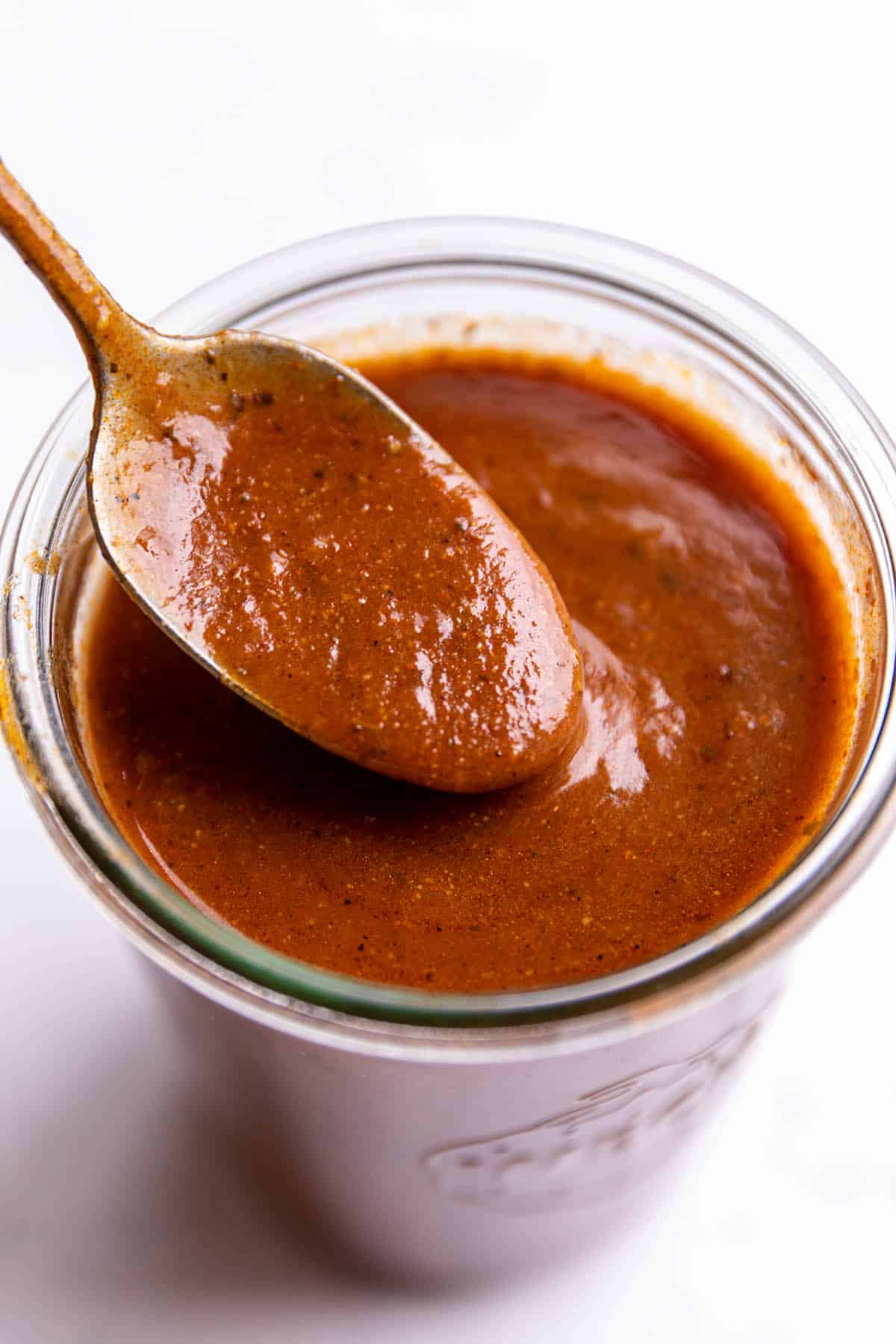 A glass weck jar with a spoon scooping out enchilada sauce.