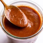 A spoon scooping enchilada sauce out of a glass jar.