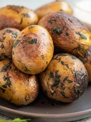 A plate with a stack of Yukon gold potatoes covered in herbs.