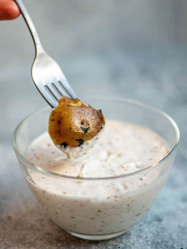 A fork with a piece of potato being dipped into a bowl of lemon garlic aioli.