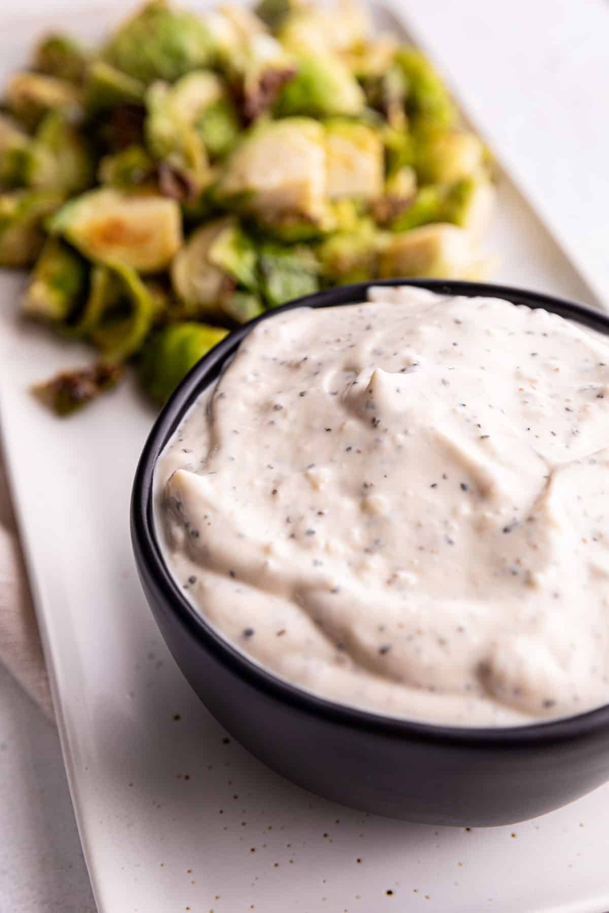 A black bowl full of a white sauce with roasted brussels sprouts.