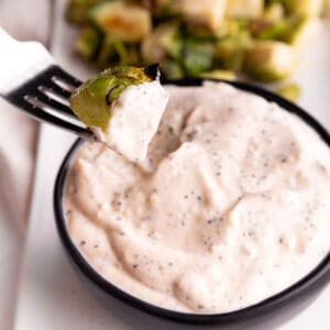 A black bowl with a white sauce and Brussels sprout being dumped in it.