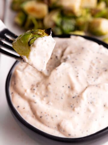 A black bowl with a white sauce and Brussels sprout being dumped in it.