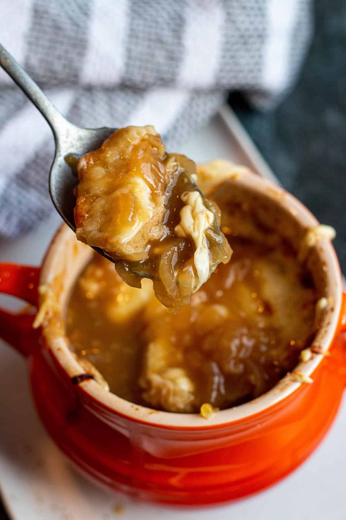 A spoon with a scoop of French onion soup being scooped out of a small soup bowl.