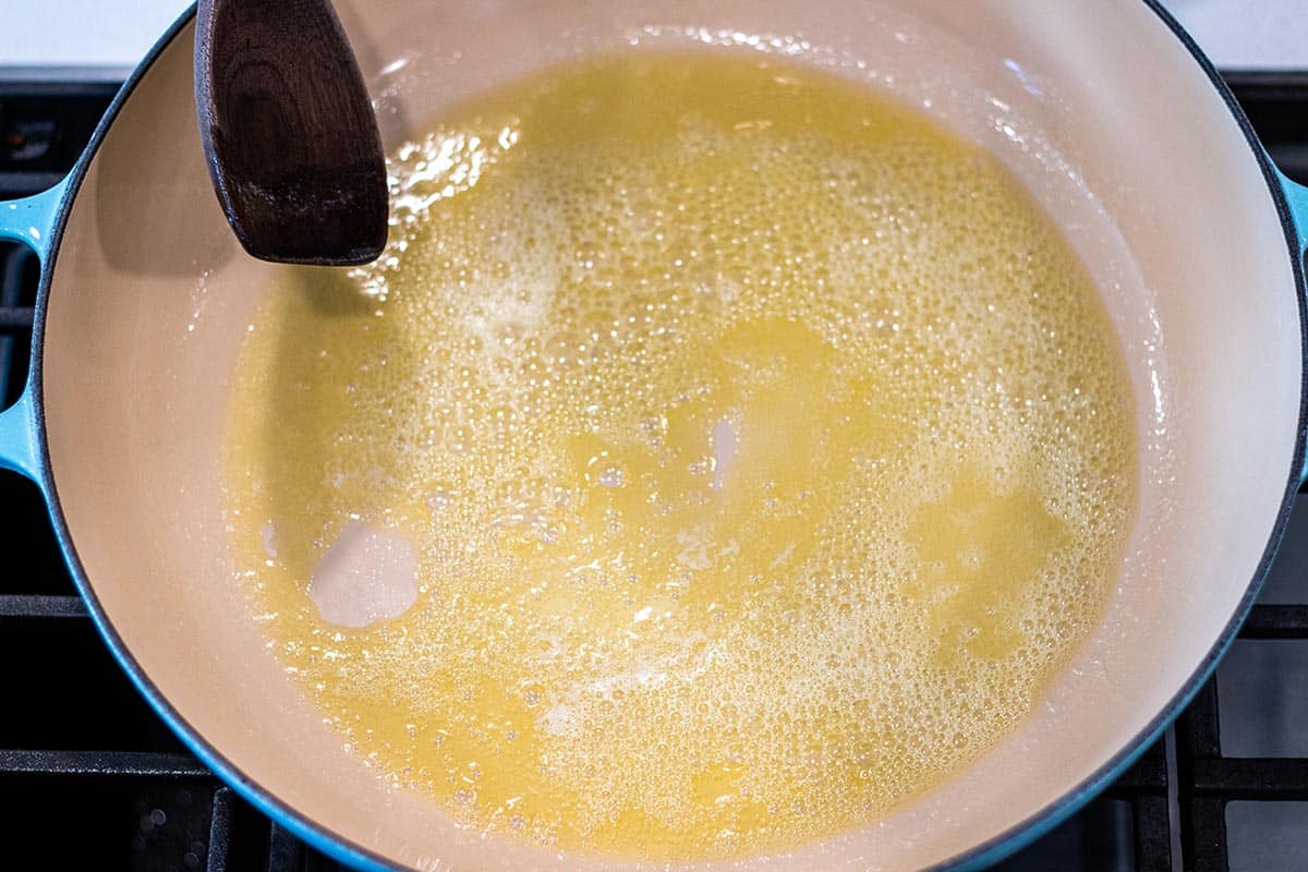 Olive oil and butter simmering in a cast iron braiser with a wooden spoon.