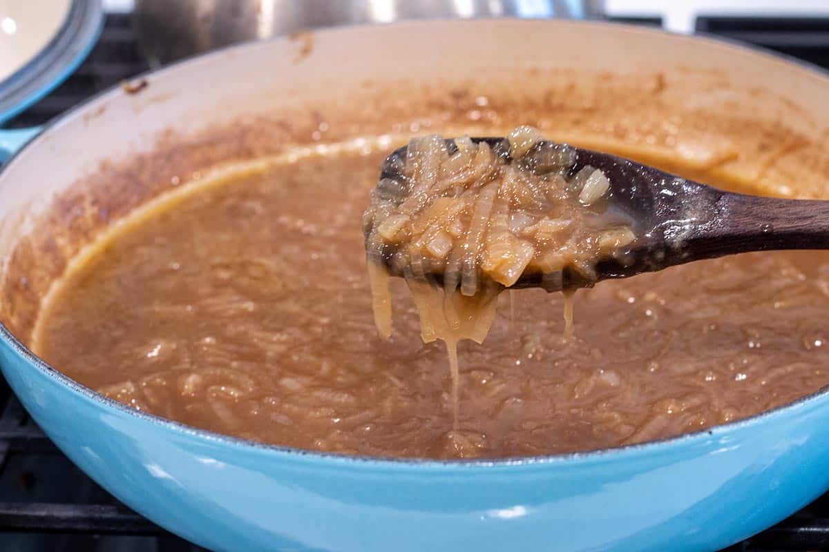 French Onion soup being simmered in a cast iron braiser with a wooden spoon.