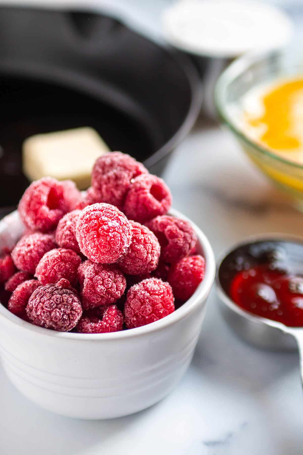 Frozen raspberries in a white bowl with a cast iron in the back. 