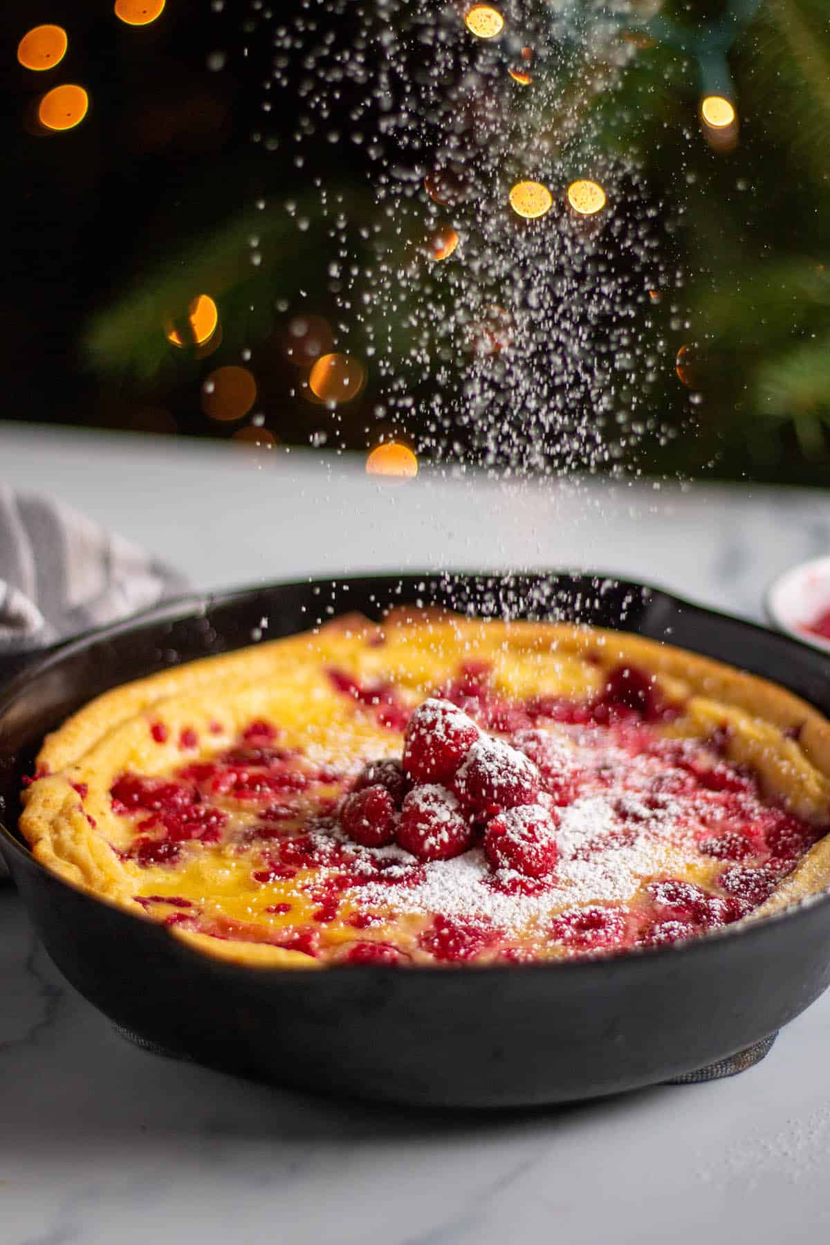 cast iron with a dutch baby and raspberries with sprinkled powder sugar.