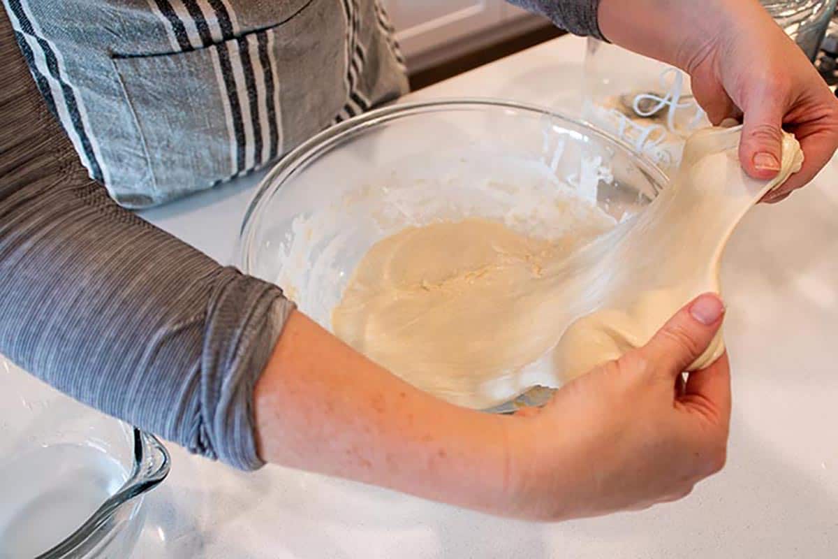 Two hands gently stretching out a ball of sourdough. 