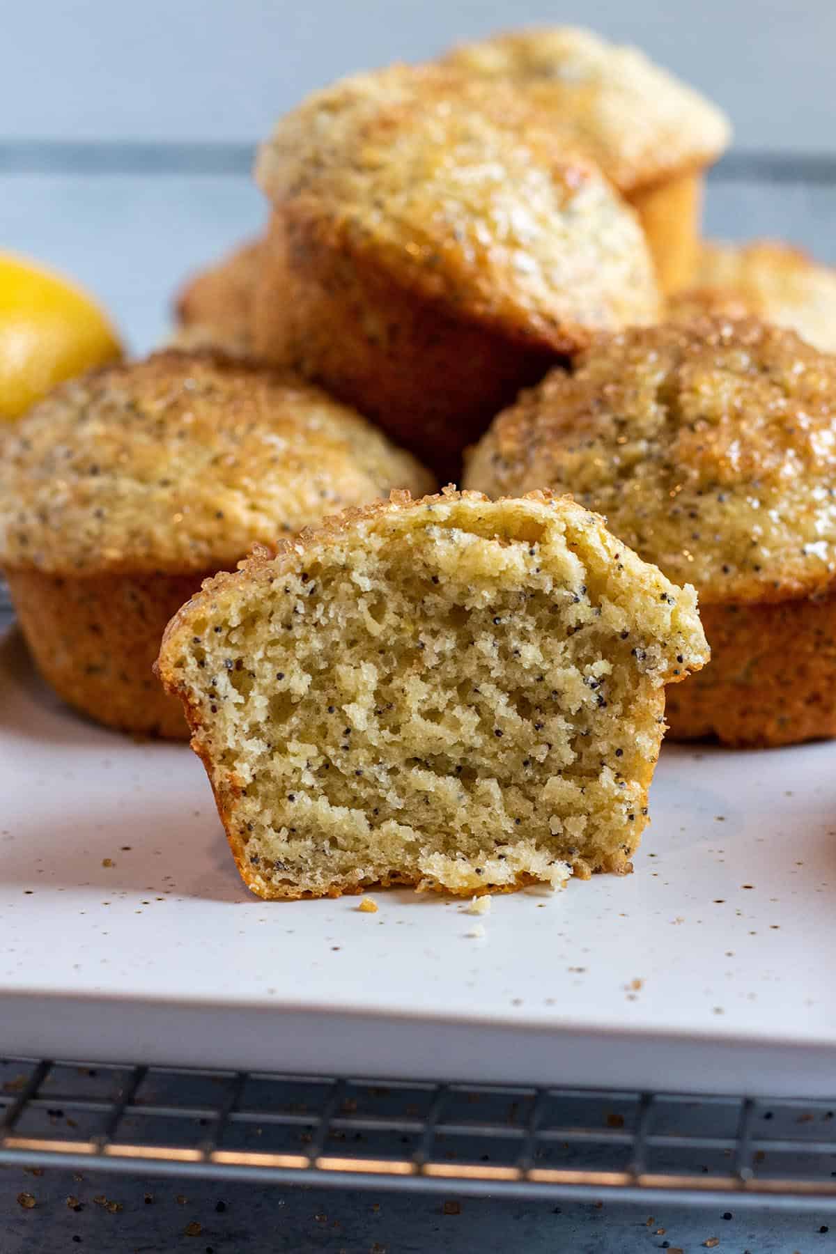 A sourdough discard lemon poppy seed muffin cut in half with full ones in the back. 