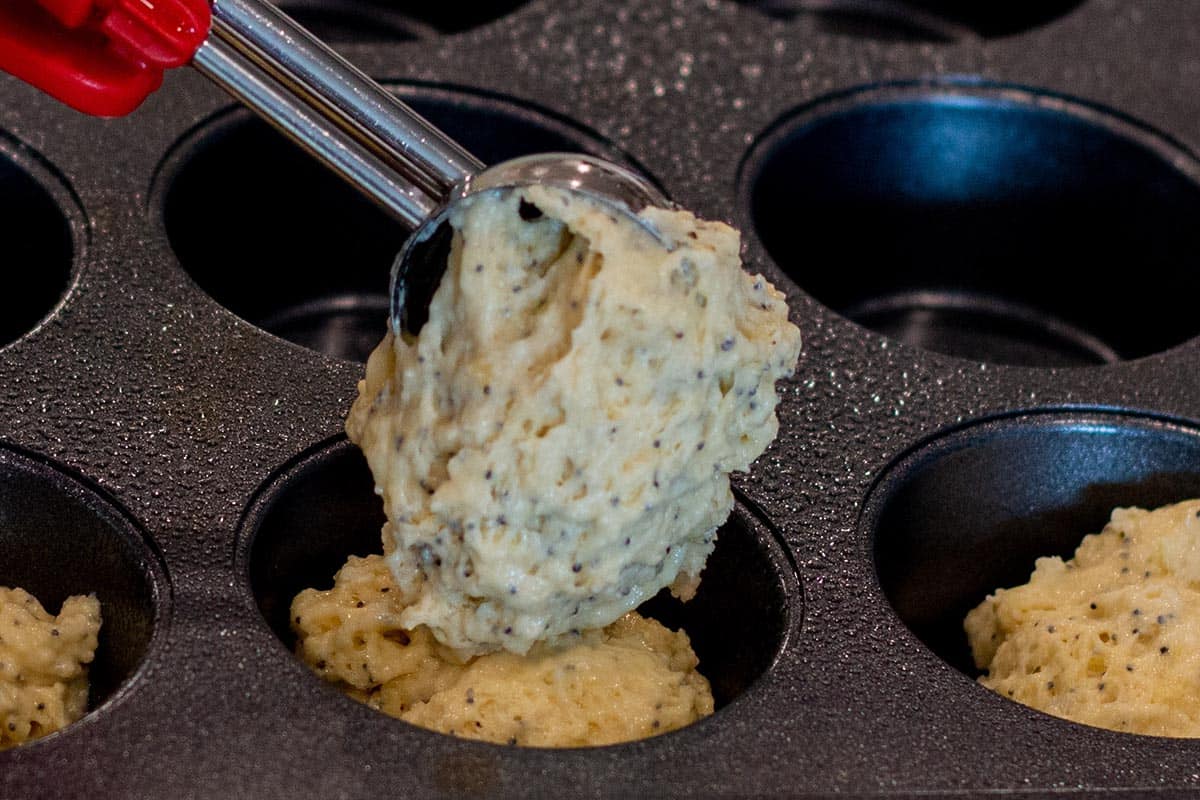 A cookie scoop spooning in the muffin batter into the muffin pan.