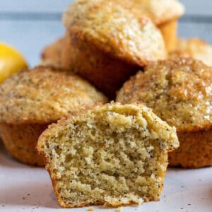 A muffin cut open and a stack of lemon poppy seed muffins in the back.