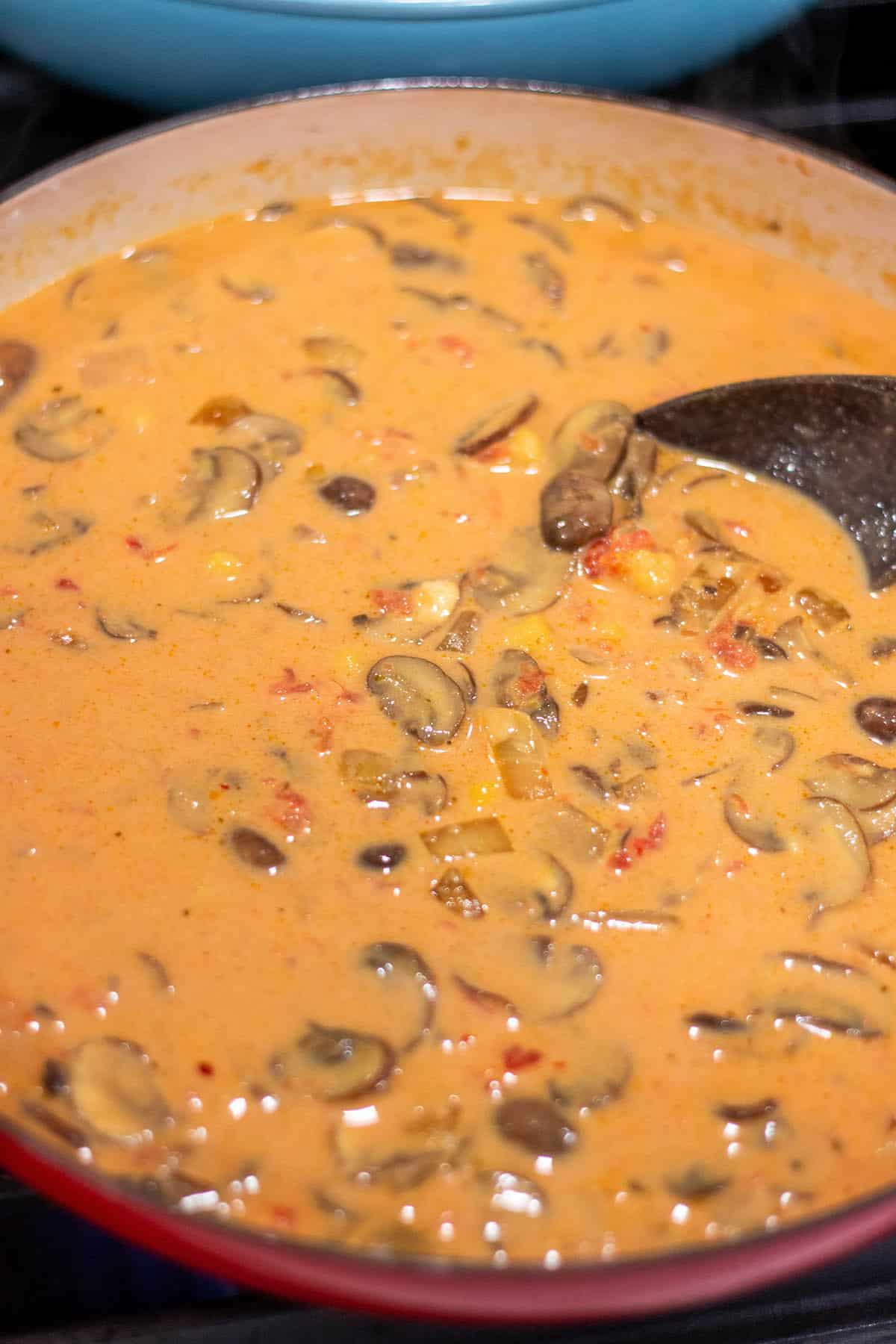 A braiser with a creamy tomato, coconut curry sauce and fresh mushrooms. Stirred together with a wooden spoon. 
