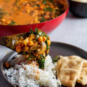 Plate with rice and naan. A wooden spoon pouring on a chickpea, spinach curry mix.
