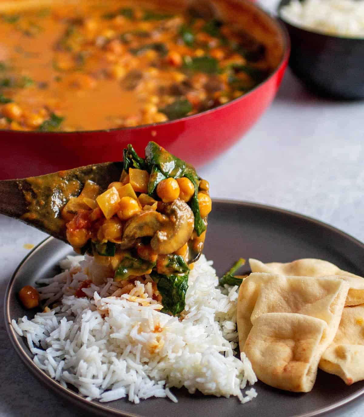 Plate with rice and naan. A wooden spoon pouring on a chickpea, spinach curry mix. 