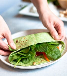 Tow halds folding over the long end of a spinach wrap.