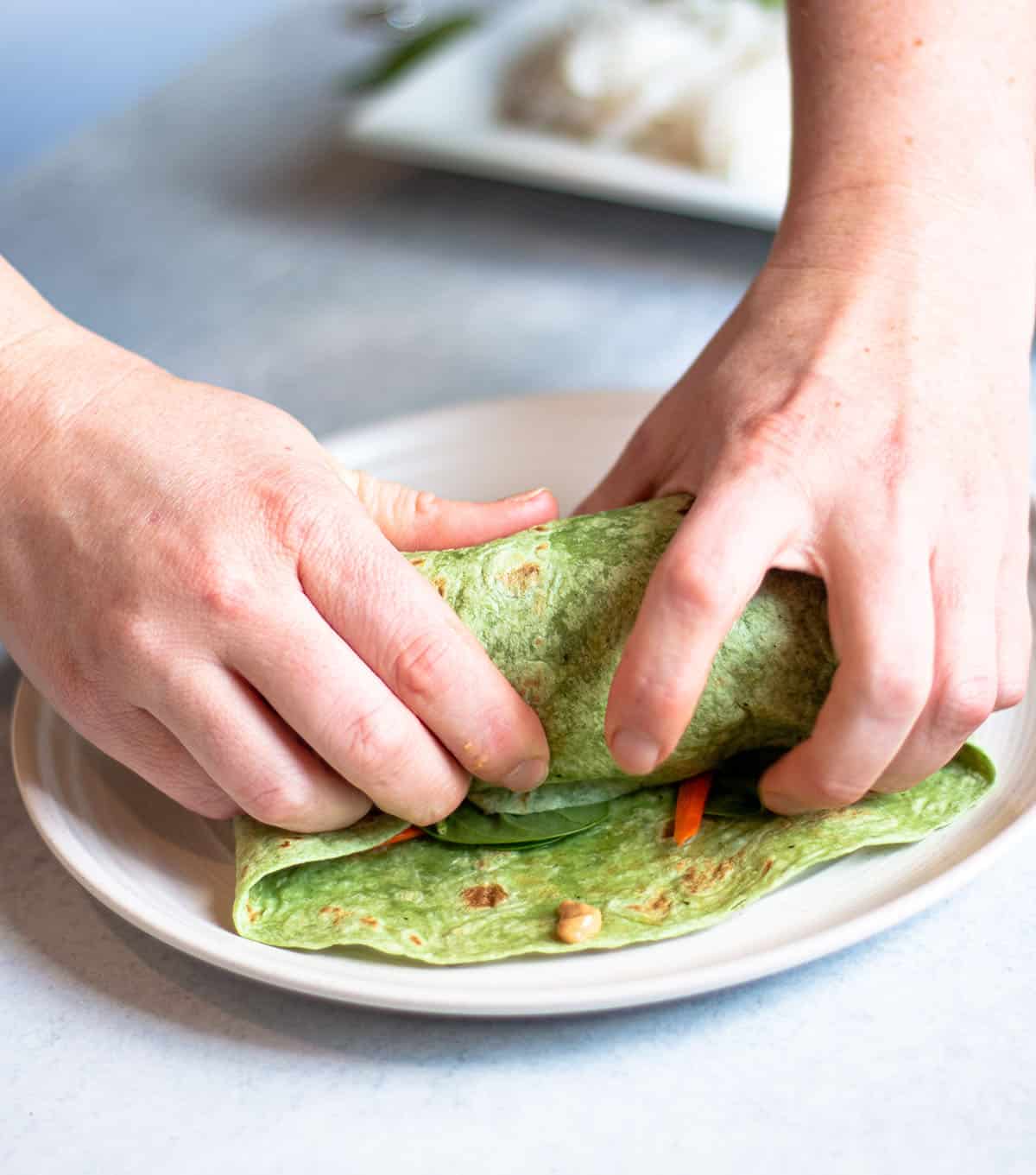 Two hands rolling up a spinach wrap.